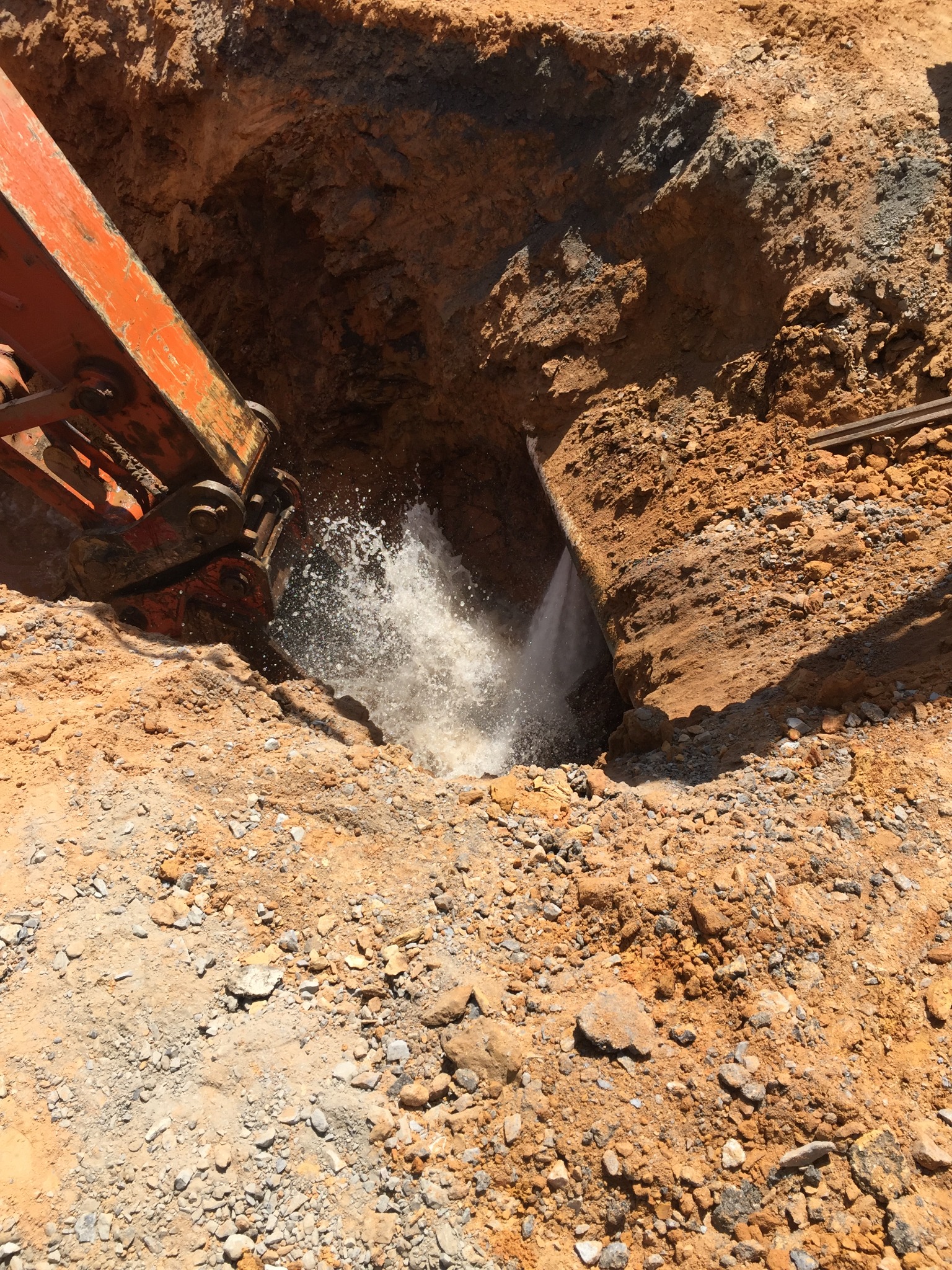 An excavator exposes a buried utility line as water sprays from the trench, illustrating a field condition that calls for hazard assessment.